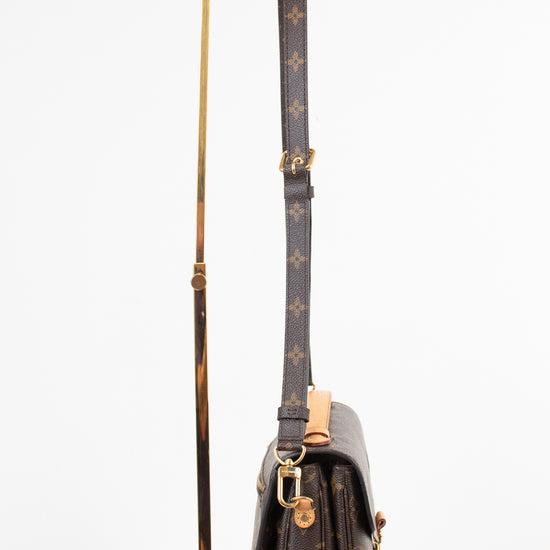 A Louis Vuitton monogram shoulder bag in dark brown coated canvas with gold-tone hardware, displayed upright on a gold metal stand against a clean white background.