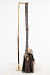 A Louis Vuitton monogram shoulder bag in dark brown coated canvas with gold-tone hardware, displayed upright on a gold metal stand against a clean white background.