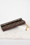 A Louis Vuitton monogram canvas long wallet or card holder with a gold-tone chain strap, resting on a white marble surface against a white background.