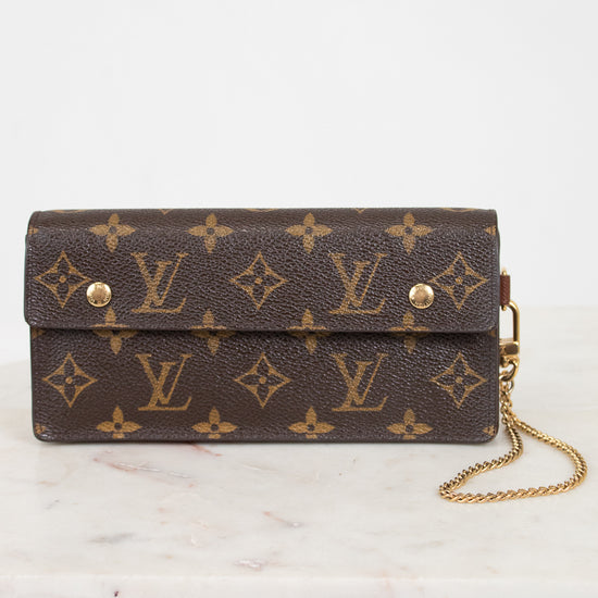 A Louis Vuitton monogram canvas clutch bag with a gold chain strap, resting on a white marble surface against a white background.