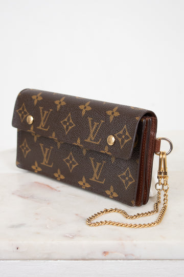 A Louis Vuitton monogram canvas clutch bag with a gold-tone chain strap, resting on a white marble surface against a white background.