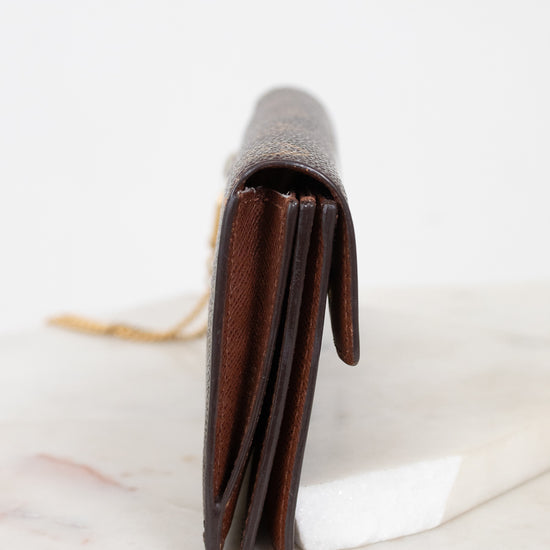 A dark brown leather bi-fold wallet standing vertically on a white marble slab against a white background.