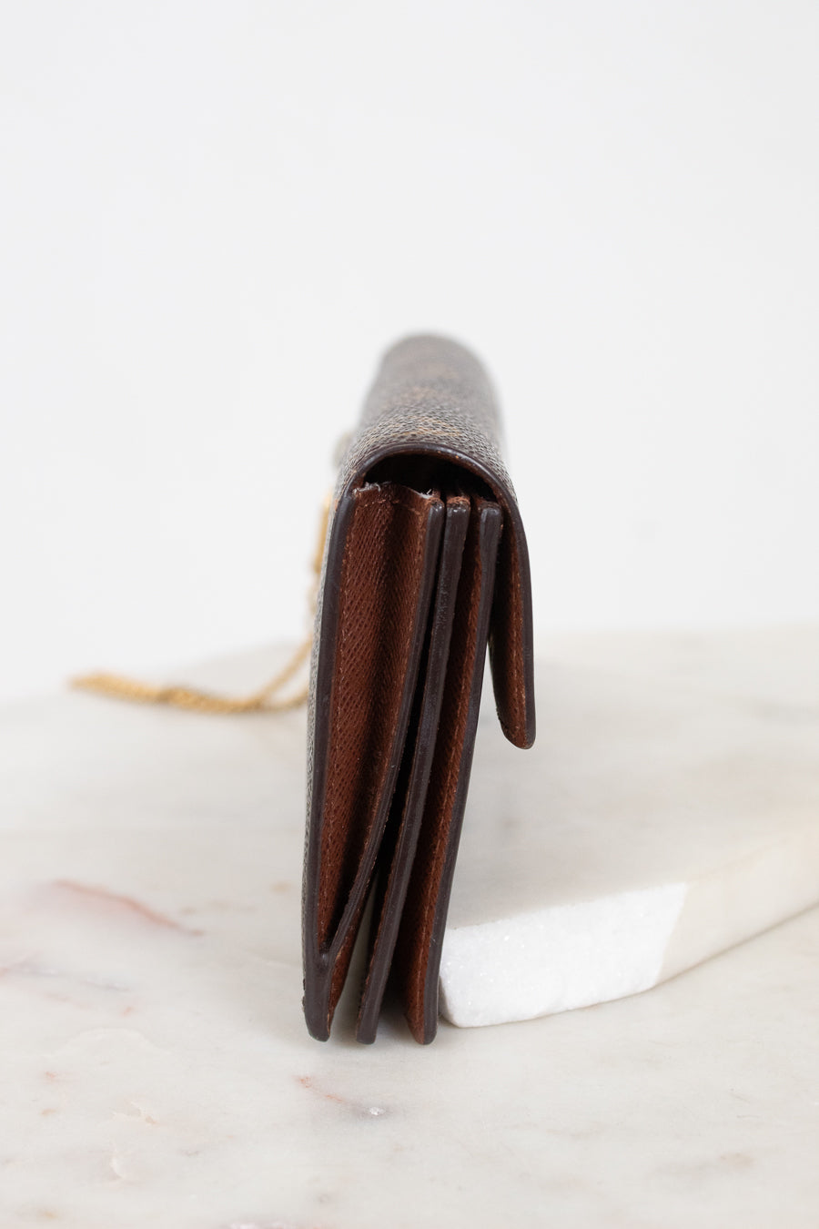 A dark brown leather bi-fold wallet standing vertically on a white marble slab against a white background.