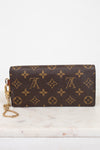 A Louis Vuitton monogram canvas wristlet clutch with a gold-tone chain strap, resting on a white marble surface against a white background.