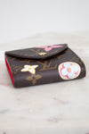 A Louis Vuitton monogram post-it note holder with decorative multi-color details, resting on a light marble surface.