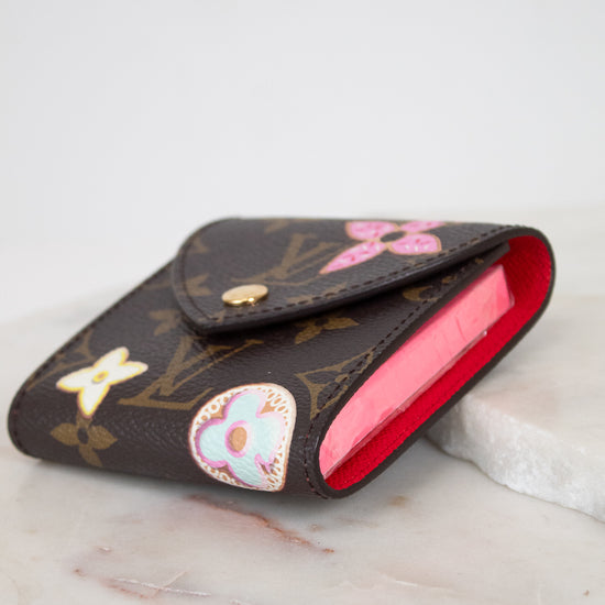 A Louis Vuitton monogram post-it note holder with a bright red interior, decorated with colorful details, resting on a white marble surface.