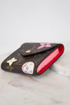 A Louis Vuitton monogram post-it note holder with a bright red interior, decorated with colorful details, resting on a white marble surface.