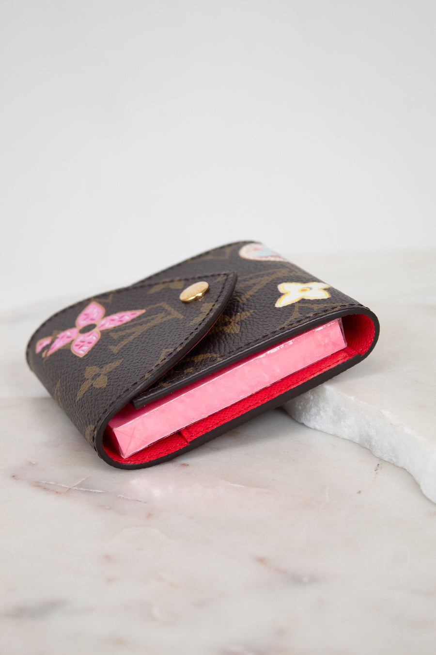 A Louis Vuitton monogram post-it note holder with multi-color accents, resting on a white marble surface against a light gray background.