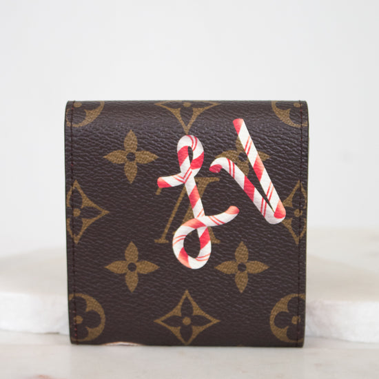 A brown monogram post-it note holder with a red and white candy cane LV design on the front, displayed on a light marble surface against a white background.