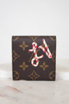 A brown monogram post-it note holder with a red and white candy cane LV design on the front, displayed on a light marble surface against a white background.