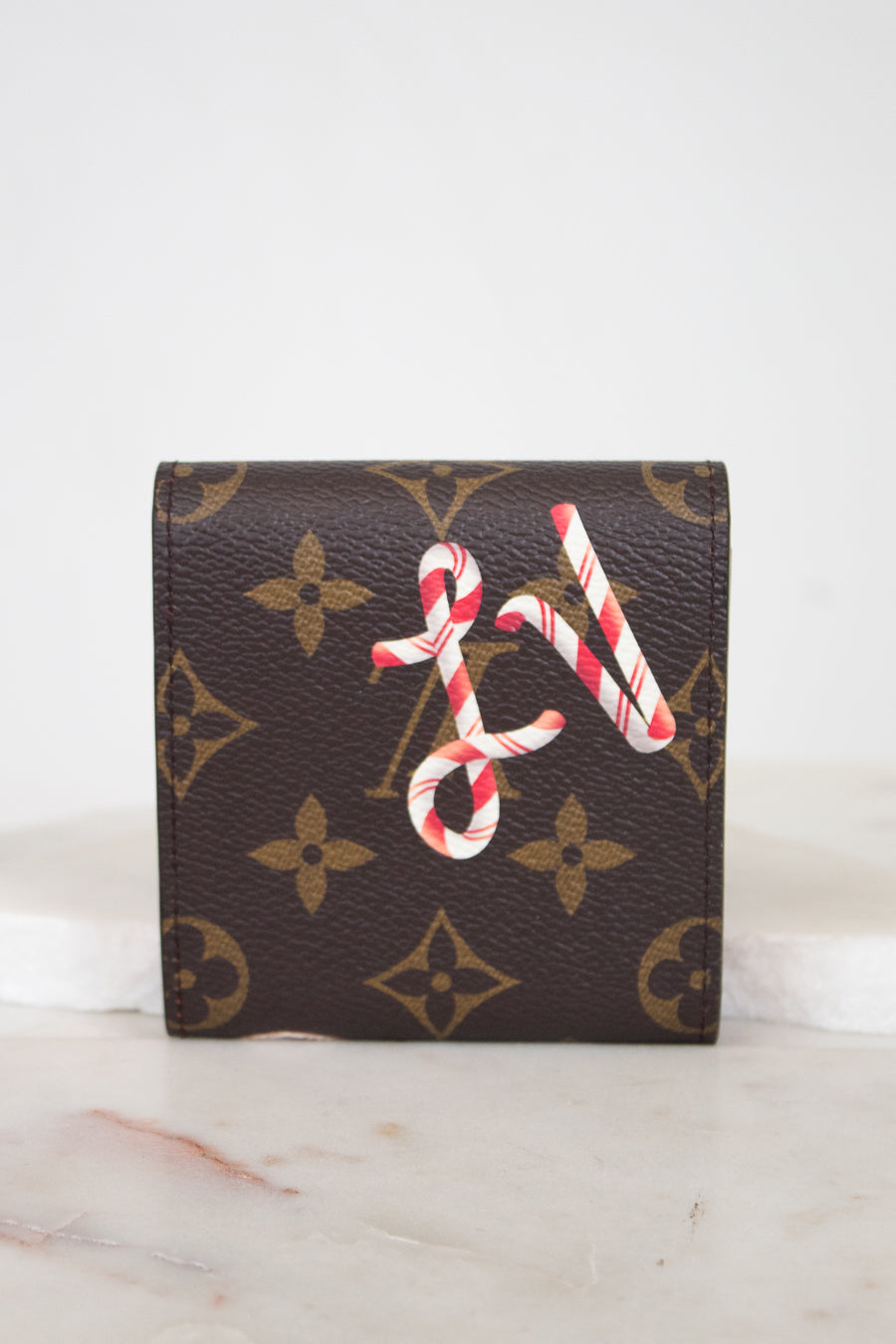 A brown monogram post-it note holder with a red and white candy cane LV design on the front, displayed on a light marble surface against a white background.