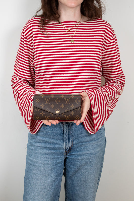 Person wearing a red and white striped shirt holding a brown wallet.