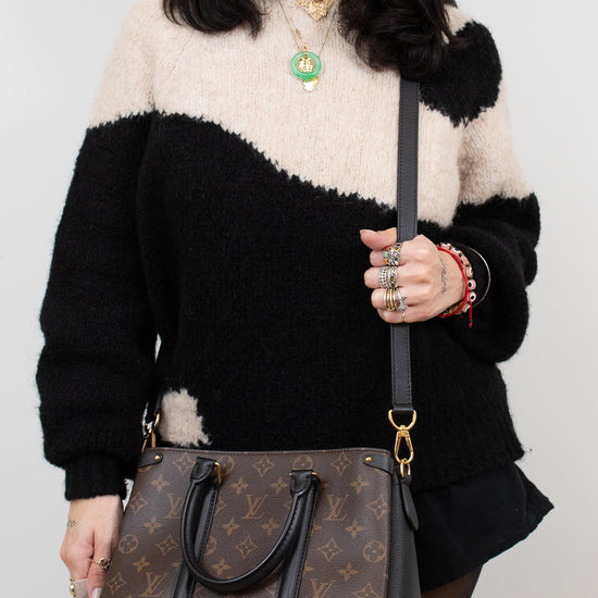 Person wearing a black and white sweater holding a brown handbag.