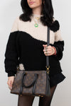 Person wearing a black and white sweater holding a brown handbag.
