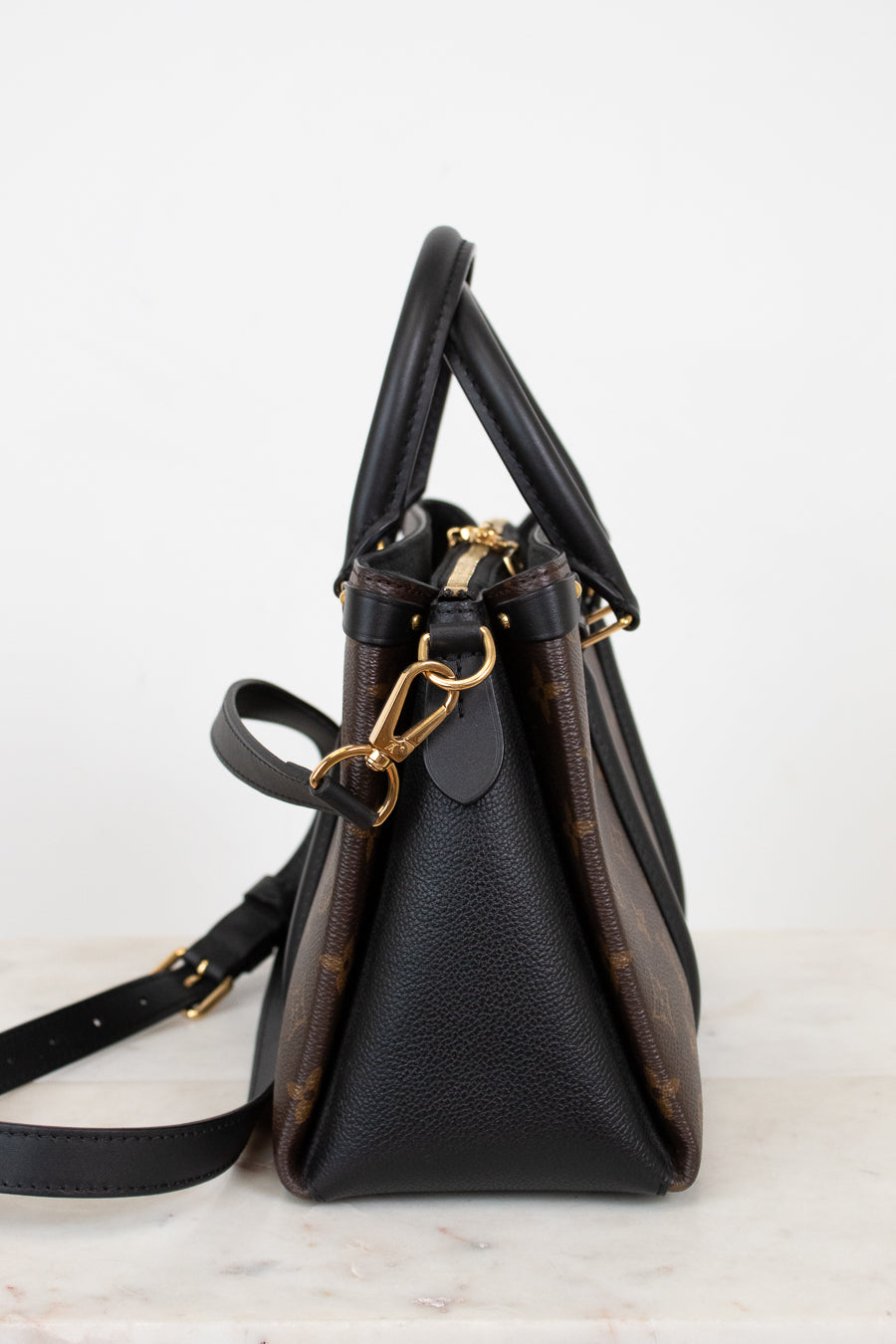 Black side panel of monogram handbag with gold accents on a light gray background