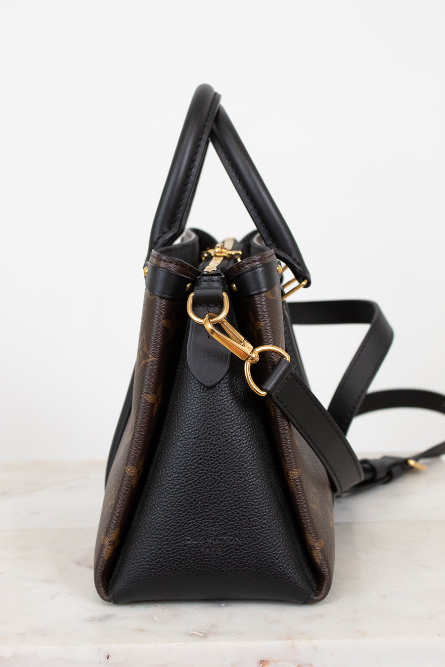 Black leather handbag with gold hardware on a light gray background