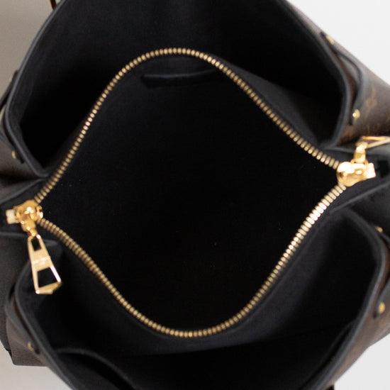 Black interior of handbag with gold zippers held open by a hand on a light gray background