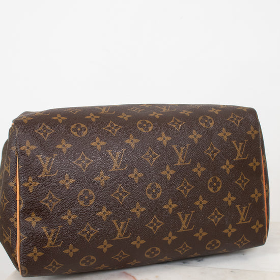 A Louis Vuitton monogram canvas shoulder bag in brown and tan, resting on a white marble surface against a white background.