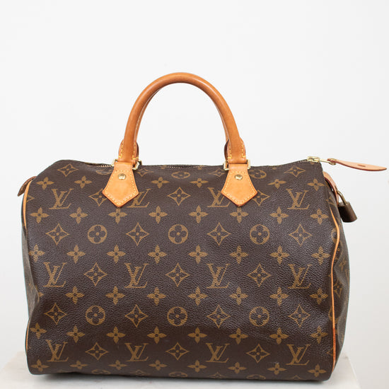 A Louis Vuitton monogram Speedy bag in brown coated canvas with tan leather handles and trim, displayed on a white marble surface against a white background.