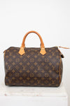 A Louis Vuitton monogram Speedy bag in brown coated canvas with tan leather handles and trim, displayed on a white marble surface against a white background.