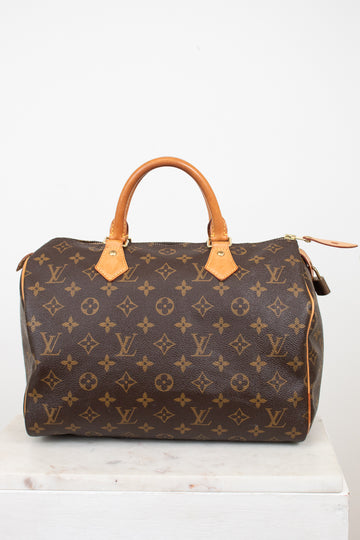 A Louis Vuitton monogram Speedy bag in brown coated canvas with tan leather handles and trim, displayed on a white marble surface against a white background.