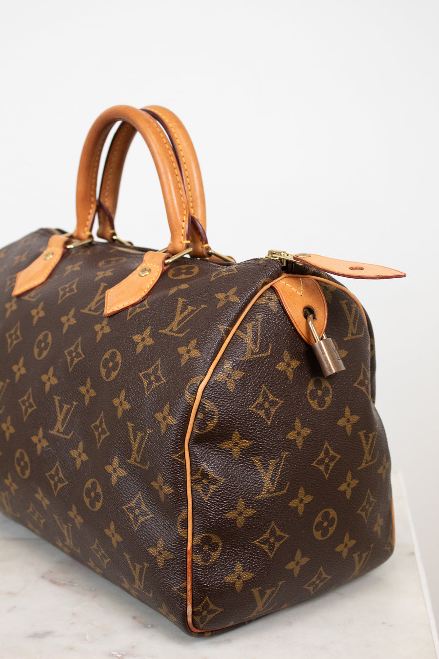 A Louis Vuitton monogram canvas Speedy handbag in dark brown with tan leather handles and trim, shown on a light gray background.