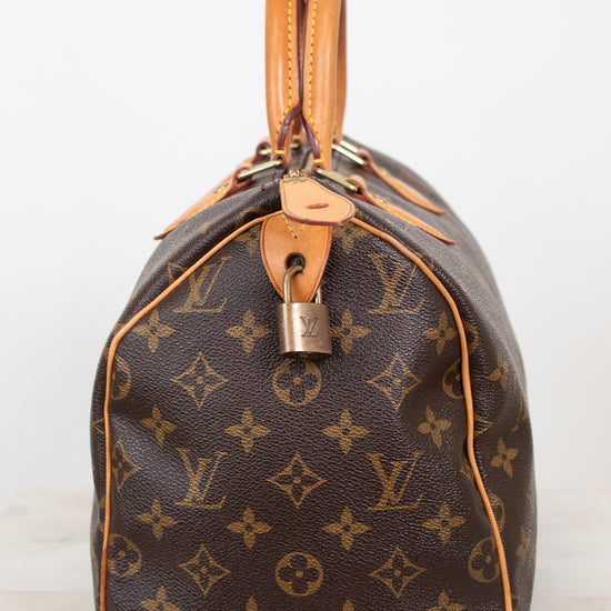 A Louis Vuitton monogram canvas Speedy bag in dark brown with tan leather trim and handles, shown from the side against a plain white background.