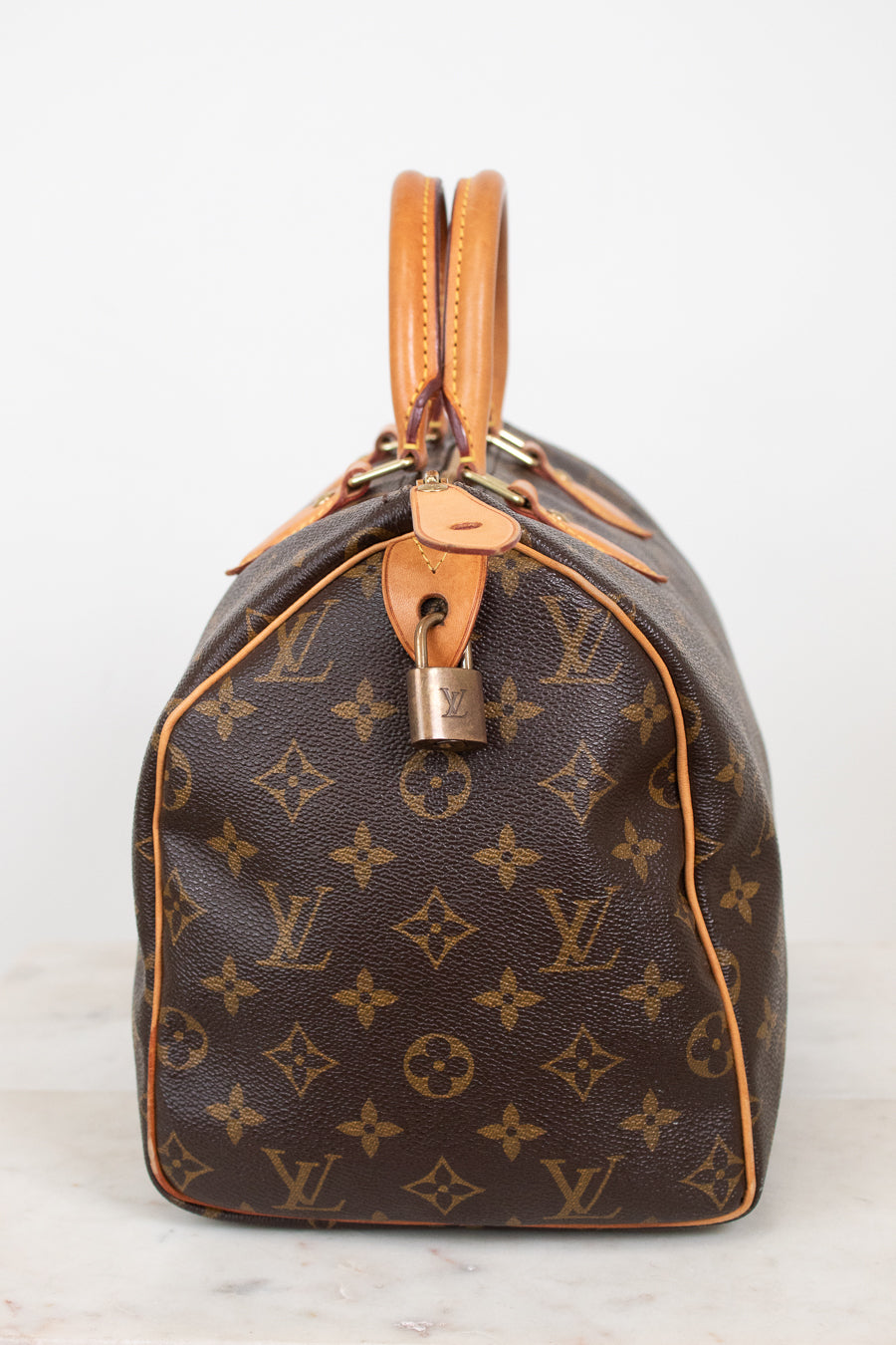 A Louis Vuitton monogram canvas Speedy bag in dark brown with tan leather trim and handles, shown from the side against a plain white background.
