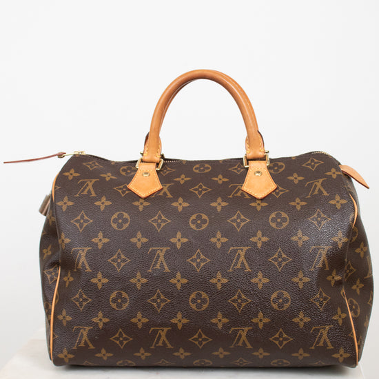 A Louis Vuitton monogram canvas Speedy handbag in dark brown with tan leather handles and trim, displayed on a white marble surface against a white background.