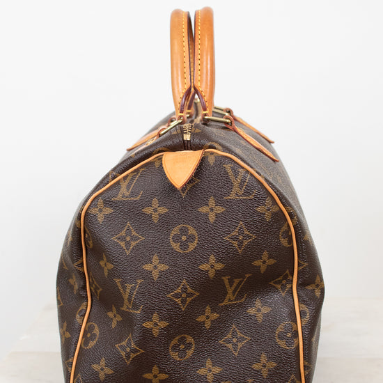 A Louis Vuitton monogram Speedy bag in brown coated canvas with tan leather trim and handles, shown from the side on a light gray background.