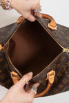 A close-up of a Louis Vuitton monogram Speedy bag being opened, showing the interior lining and gold-tone hardware, with hands holding the zipper tabs.