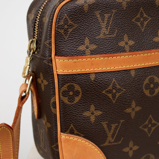 Louis Vuitton monogram coated canvas crossbody bag in dark brown with tan leather trim and gold-tone hardware, shown on a light neutral background.
