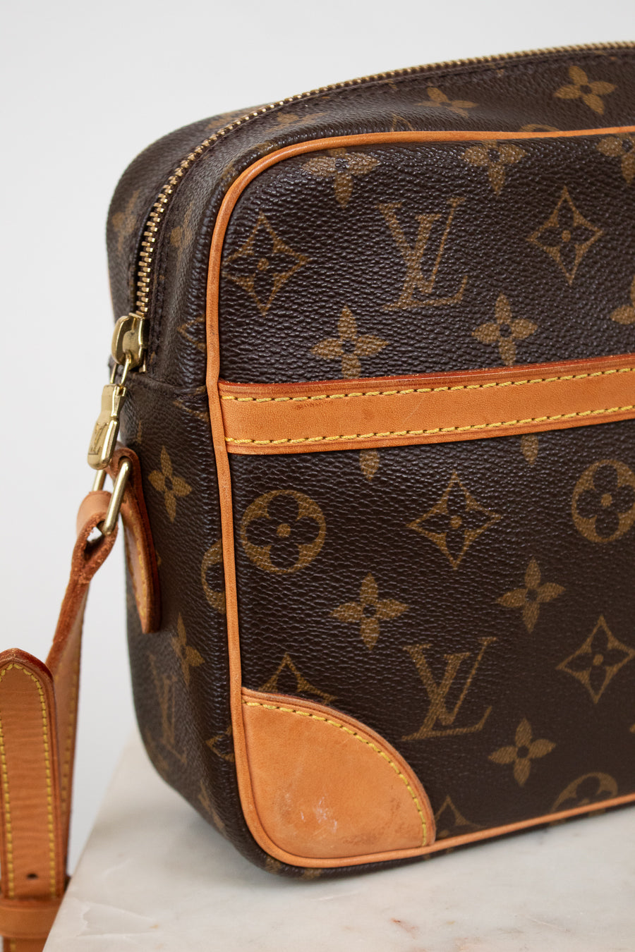 Louis Vuitton monogram coated canvas crossbody bag in dark brown with tan leather trim and gold-tone hardware, shown on a light neutral background.