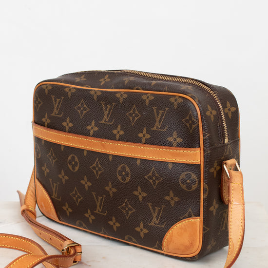 A Louis Vuitton monogram coated canvas crossbody bag with tan leather trim and strap, displayed on a light marble surface against a white background.