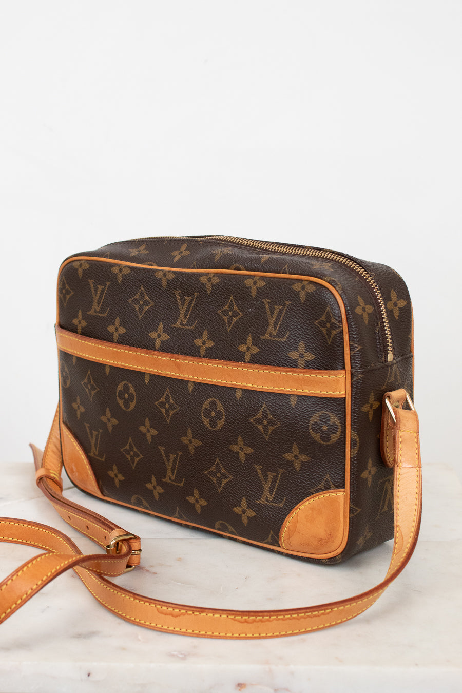 A Louis Vuitton monogram coated canvas crossbody bag with tan leather trim and strap, displayed on a light marble surface against a white background.