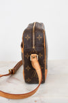 A Louis Vuitton monogram coated canvas crossbody bag shown from the side profile, featuring the classic brown and tan monogram pattern with a gold-tone zipper and leather strap on a light marble surface.