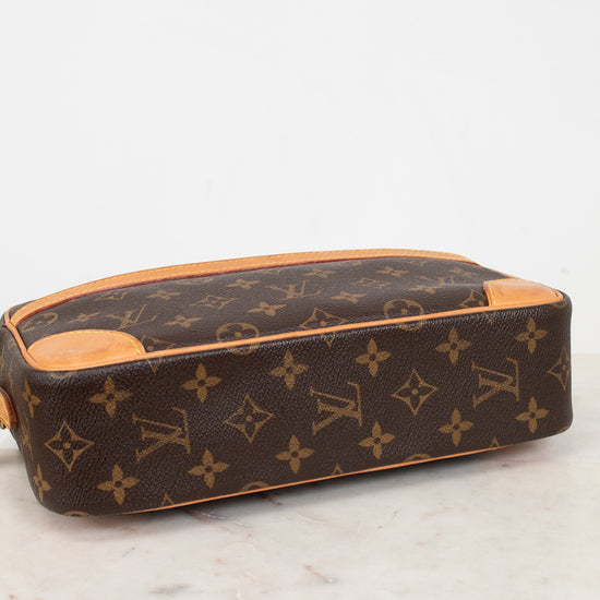 A Louis Vuitton monogram coated canvas handbag with tan leather trim viewed from the bottom, resting on a white marble surface against a white background.