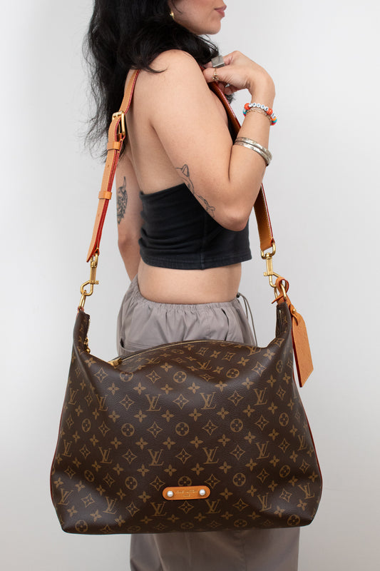 Person holding a brown monogram handbag against a white background