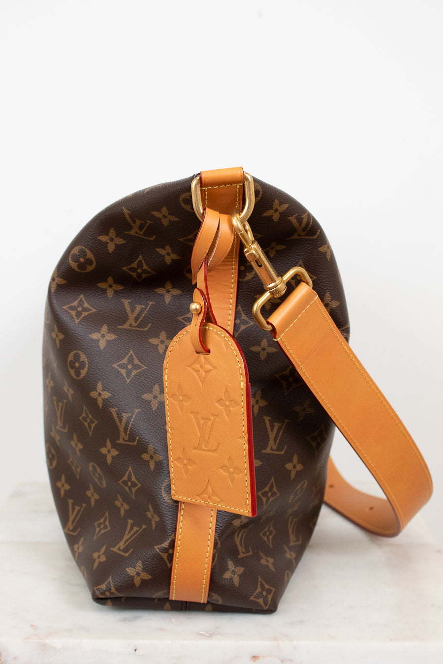 Louis Vuitton monogram handbag with tan leather strap on a white background