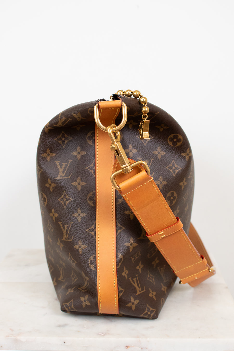 Louis Vuitton handbag with monogram pattern and brown strap on a white background