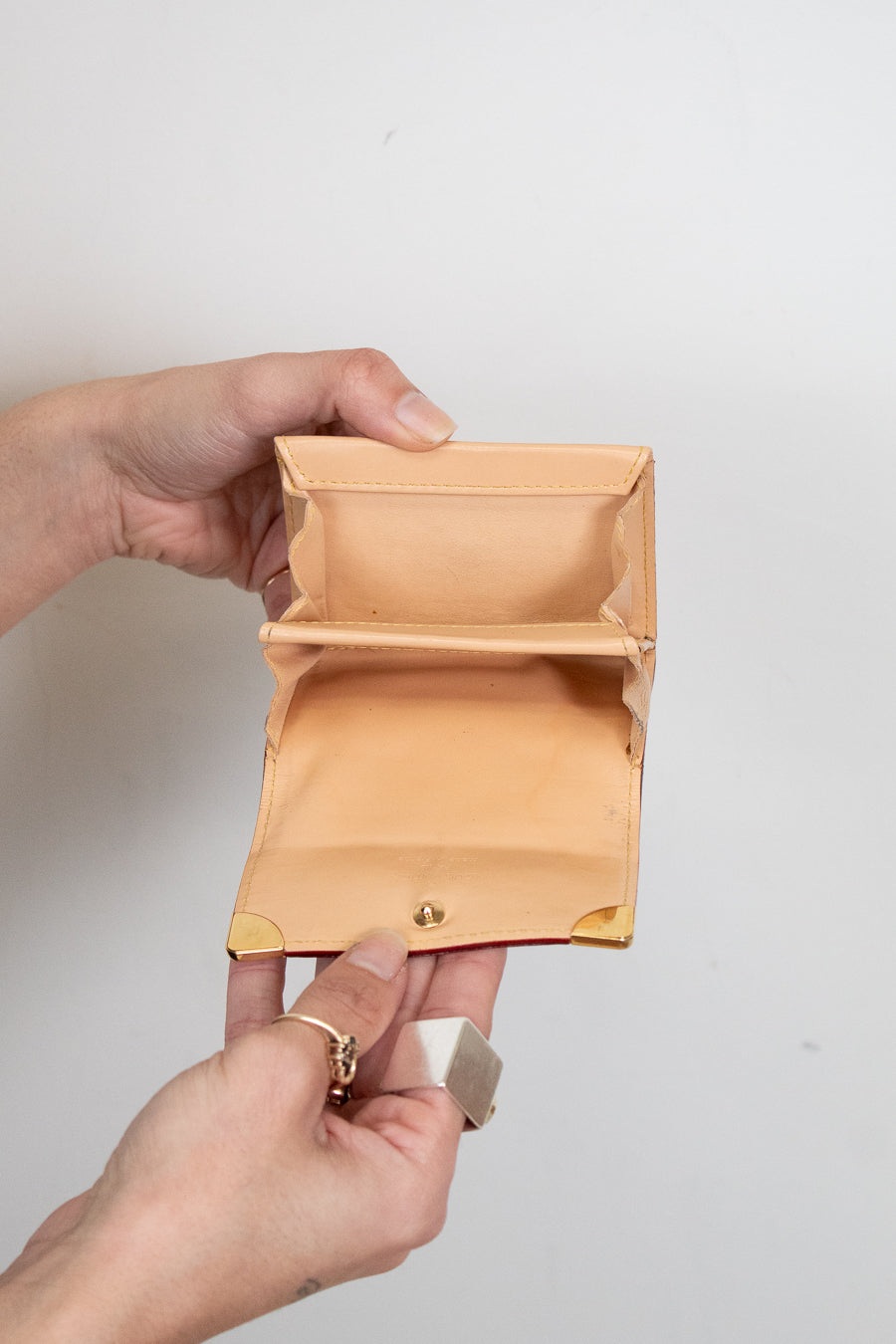Hand holding an empty beige wallet against a plain background