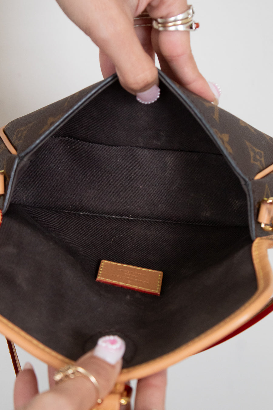 Close-up of a hand holding an open brown leather handbag with visible brand logo.