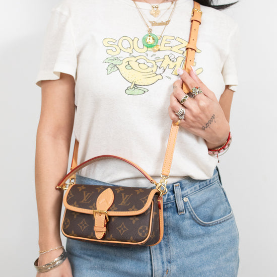 Person wearing a white t-shirt with a graphic design, blue jeans, and holding a brown handbag.
