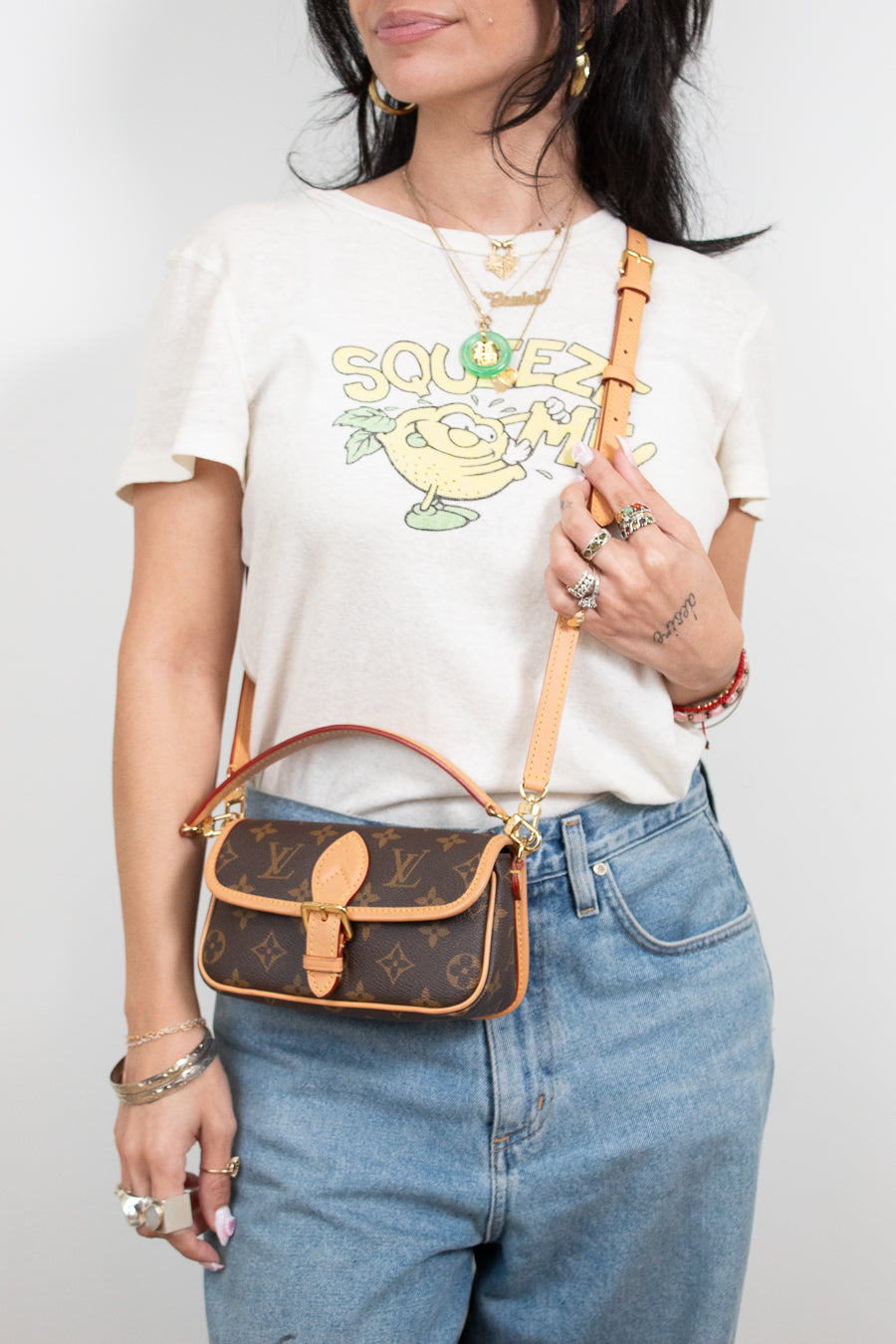 Person wearing a white t-shirt with a graphic design, blue jeans, and holding a brown handbag.
