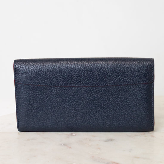A dark navy blue pebbled leather wallet standing upright on a light marble surface against a white background.