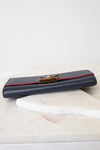 A navy blue leather clutch wallet with a red accent stripe and a gold-tone metal clasp, resting on a white marble slab against a white background.