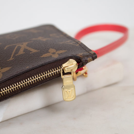 A close-up of a Louis Vuitton monogram canvas zip pouch with a gold-tone zipper pull and a bright red wristlet strap, resting on a white marble surface.