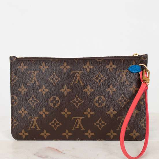 A Louis Vuitton monogram canvas wristlet pouch with a brown and tan pattern, featuring a bright red wrist strap and a small blue attachment detail.