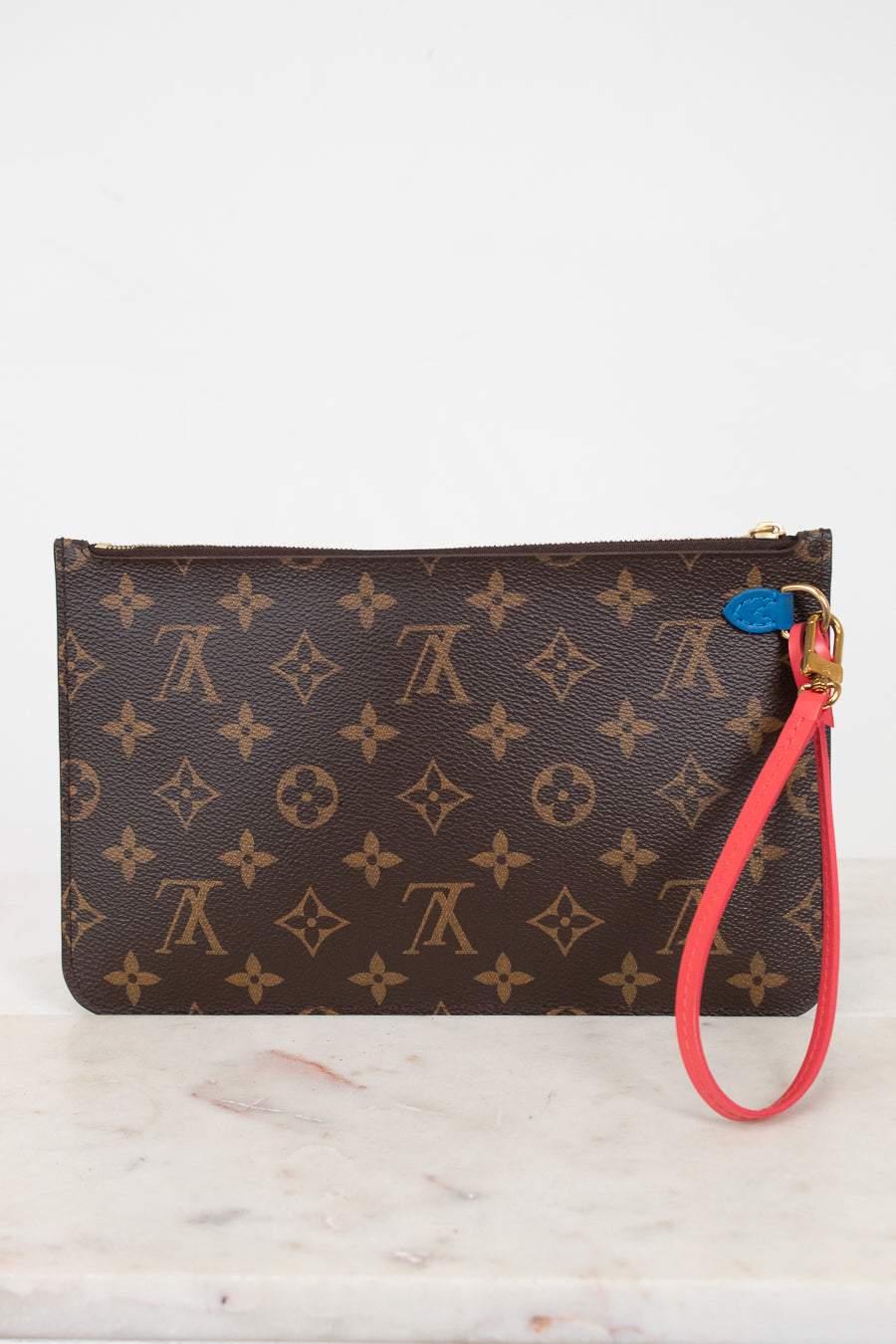 A Louis Vuitton monogram canvas wristlet pouch with a brown and tan pattern, featuring a bright red wrist strap and a small blue attachment detail.