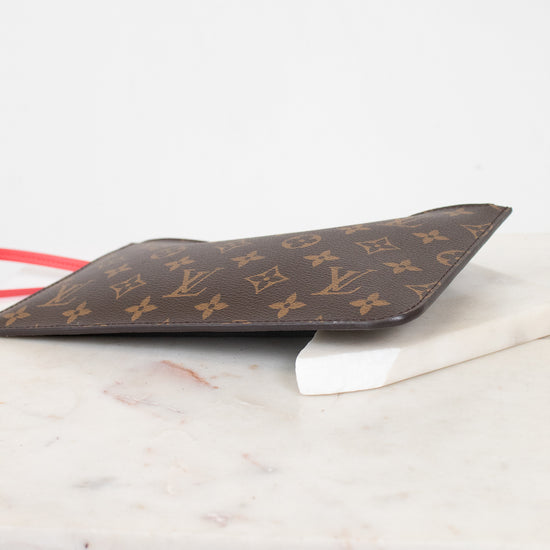 A Louis Vuitton monogram canvas small pouch in dark brown with gold LV logos, resting on a white marble surface against a white background.